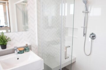 A bathroom's shower with a chrome tap, transparent glass doors, and a shelf.
