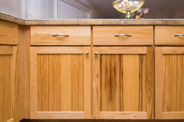 A set of bottom kitchen cabinets in a maple finish with updated hardware such as pull knobs and handles.