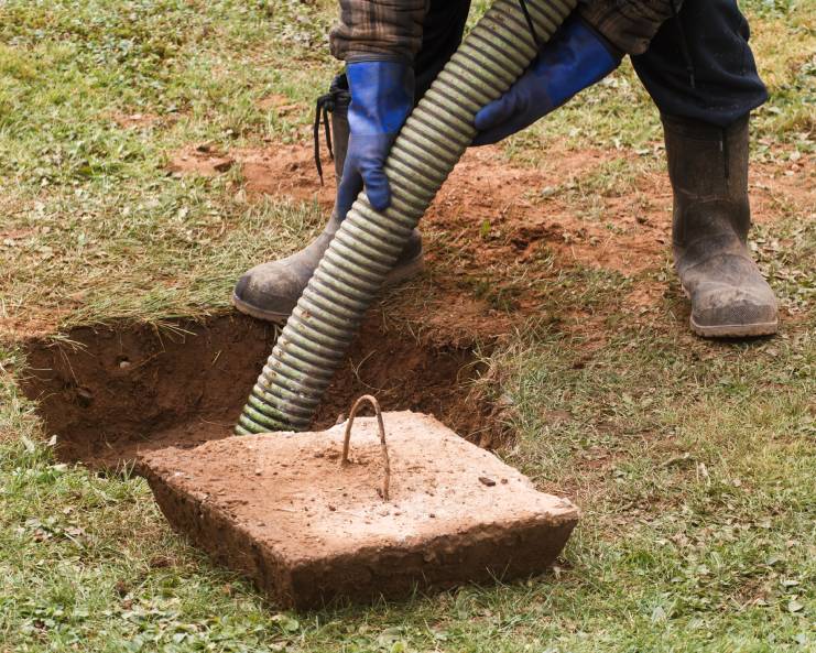 A residential septic tank is being serviced by a professional waste management worker with gloves and boots on.