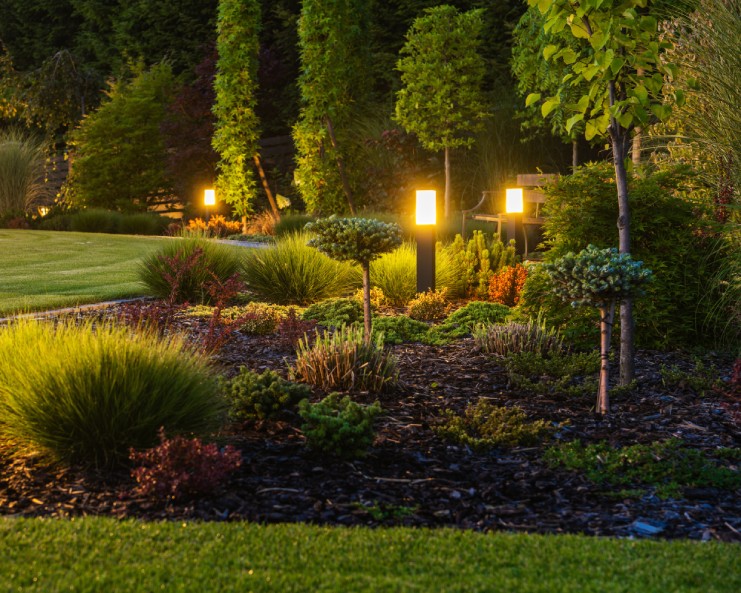 A small outdoor garden space with paver lighting and ornaments placed throughout the greenery. It's dark outside.