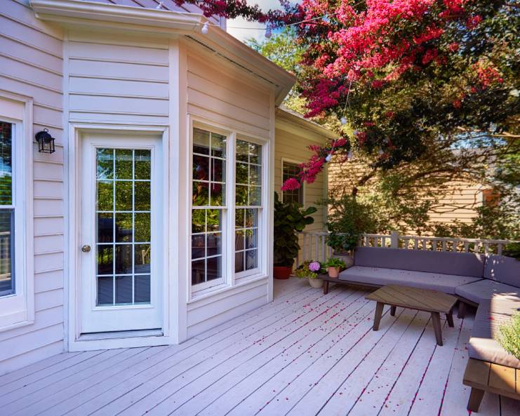 A cozy patio with a several potted plants, pieces of outdoor furniture, and a large, pink, flowering tree.