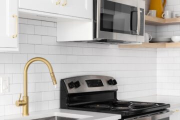 A modern kitchen with subway tiles, a gold faucet and cabinet hardware, and stainless steel appliances.