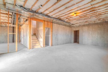 An unfinished basement displays concrete walls, silver HVAC ducts, wooden framing, and gray insulation.