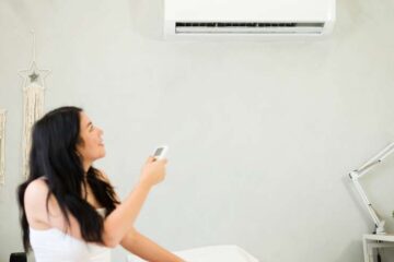 A young woman in shorts and a t-shirt is seen using a remote to adjust the temperature of her mini split unit.