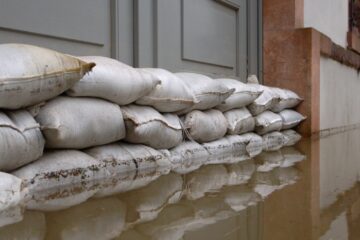 A collection of sandbags stacked up outside of a property. There is sitting water at the base of the sandbag wall.