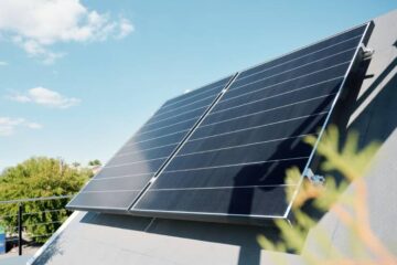 Two large solar panels installed on a roof. There is a wooden planter near the solar panels on the roof.