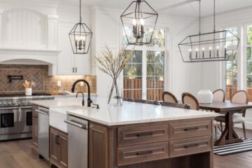 A beautiful kitchen in a luxurious home with hanging light fixtures and marble countertops, along with stainless steel appliances.