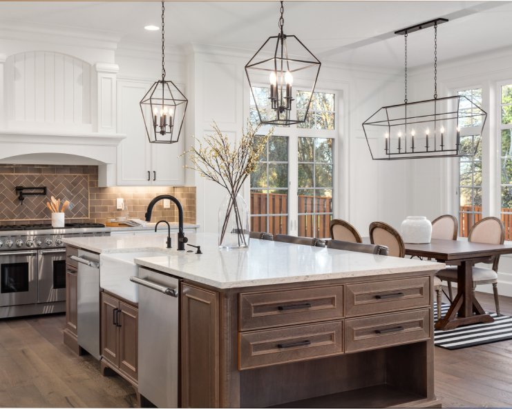 A beautiful kitchen in a luxurious home with hanging light fixtures and marble countertops, along with stainless steel appliances.