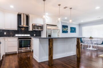 A bright open-concept kitchen with polished dark wood floors and an island with wood posts holding the breakfast bar.