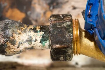 A corroded pipe with a bulge, up close. A newer pipe fitting made of a different metal is screwed into the old pipe.