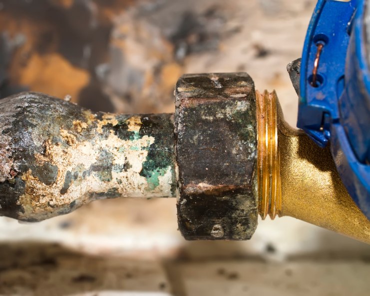A corroded pipe with a bulge, up close. A newer pipe fitting made of a different metal is screwed into the old pipe.