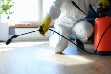 A professional rodent control specialist in protective gear performing extermination services inside of a home.