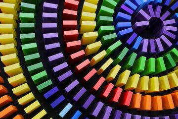 Many square objects in the colors of the rainbow stand up in a spiral design with purple in the middle.