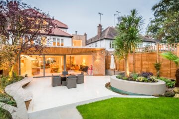 A villa with a patio features warm lighting and trees that accent the space. The inside of the home is visible.