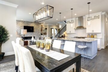 An open layout of a home displays a black dining room table with white chairs, white kitchen cabinets, and a large island.