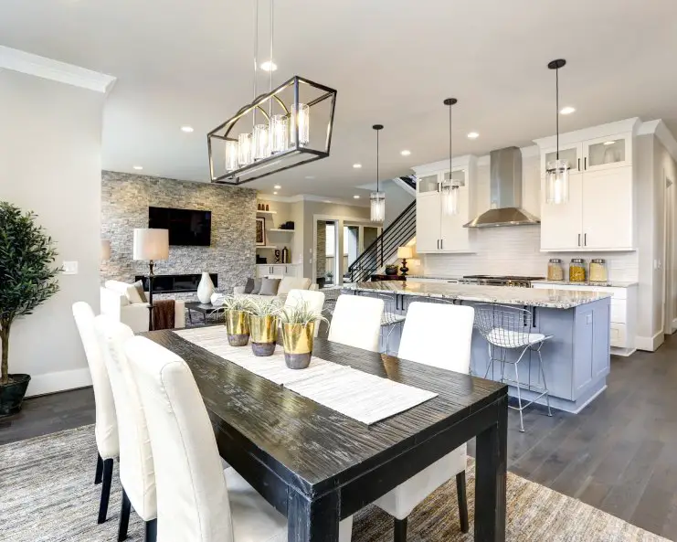 An open layout of a home displays a black dining room table with white chairs, white kitchen cabinets, and a large island.