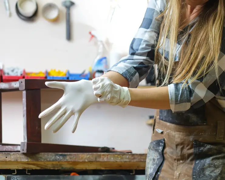 A person putting on and stretching a white glove on their hand. She has her sleeves rolled up to her elbows.