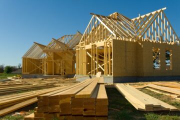 A view low from the ground, with long planks of lumber on the ground and a half-built house during the construction process.