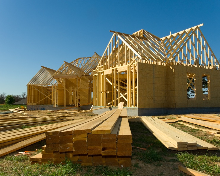 A view low from the ground, with long planks of lumber on the ground and a half-built house during the construction process.