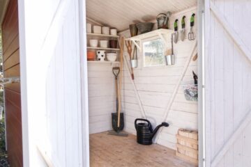 A small shed with the doors open and organization systems on the walls. The summer yard tools are hanging on the wall.