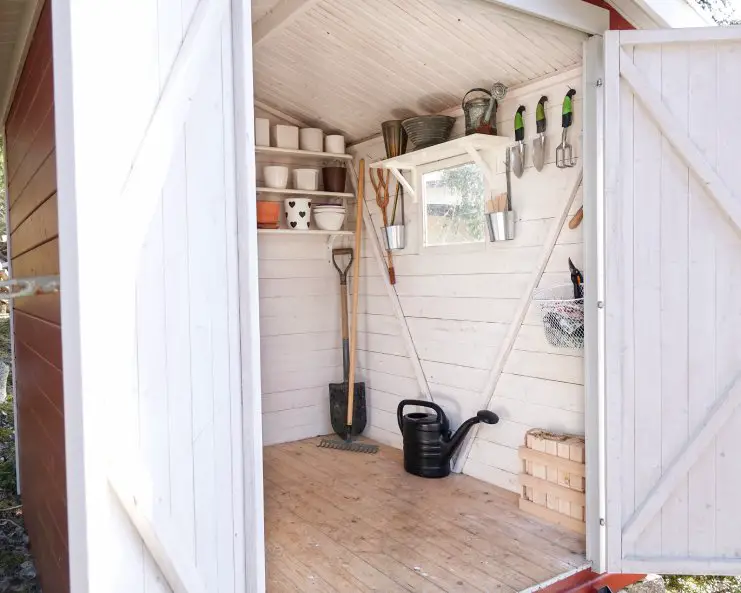 A small shed with the doors open and organization systems on the walls. The summer yard tools are hanging on the wall.