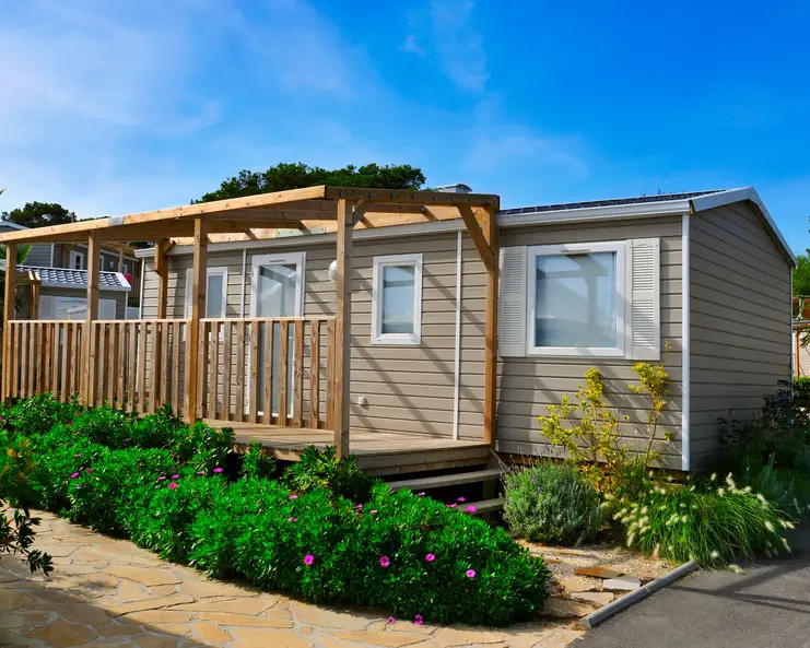 A mobile home with a pergola-style deck and well-tended landscaping with a stone pathway throughout.