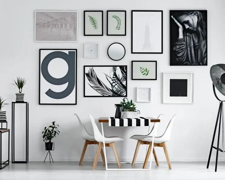 A dining table placed against the wall which is filled with white and black wall art. Next to it are small potted plants.