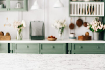 An empty countertop with a marble surface in a monochrome kitchen with green wooden cabinets and silver accents.