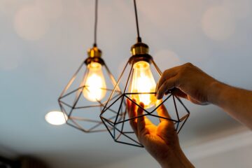 A person installs modern geometric pendant light fixtures with warm Edison bulbs in their home.