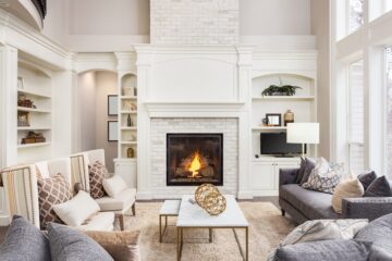 A beautiful modern living room with gray furniture and white sitting chairs. There is a brick wall fireplace focal point.