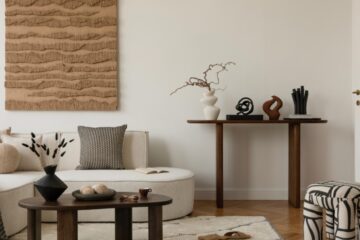 A living room with a curved white sofa, a dark wood coffee table and side table, a beige rug, and a textured piece of art.