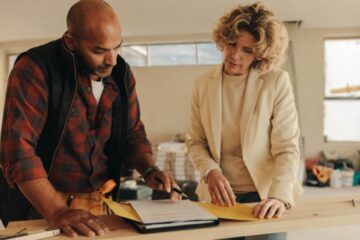 A contractor and homeowner review warranty paperwork in a binder together during a home renovation project.