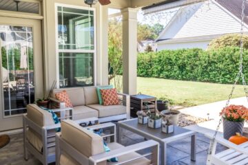 A covered patio off the backdoor of the house. The patio has a ceiling fan and patio furniture facing the backyard.