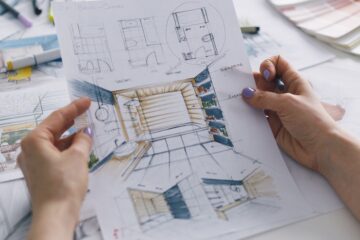 A person holding blueprints for a residential bathroom remodel in their hands. The person wears purple nail polish.