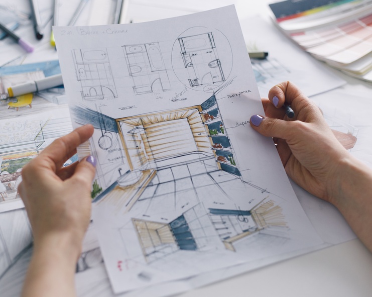 A person holding blueprints for a residential bathroom remodel in their hands. The person wears purple nail polish.