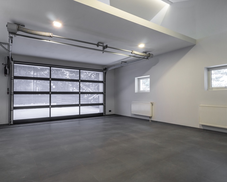 An interior view of a modern home garage with a large glass door, a grey floor, and white-painted walls.