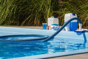 A close-up of a residential in-ground swimming pool with various pool chemicals and cleaning supplies along the edge.