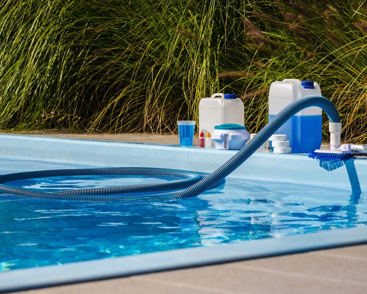 A close-up of a residential in-ground swimming pool with various pool chemicals and cleaning supplies along the edge.