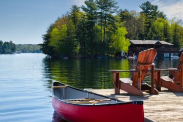 Two chairs on a wooden dock that looks out over a peaceful lake. There is also a canoe attached to the dock.