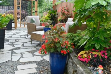 A colorful backyard patio with stone pavers, outdoor seating, flowering plants, and a decorative wooden garden gate.