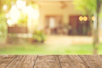 A shot of a backyard that is partially blurry. There is a home in the background of the image and a wood surface in the foreground.