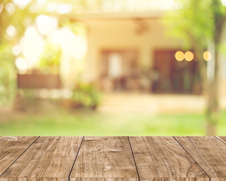 A shot of a backyard that is partially blurry. There is a home in the background of the image and a wood surface in the foreground.