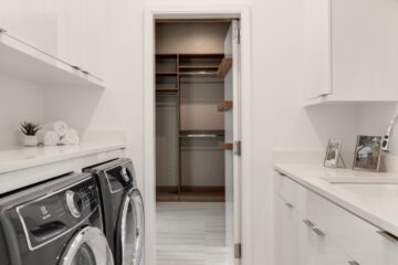 A home's laundry room features white walls, a sink, and a washer and dryer that sit side by side under a counter.