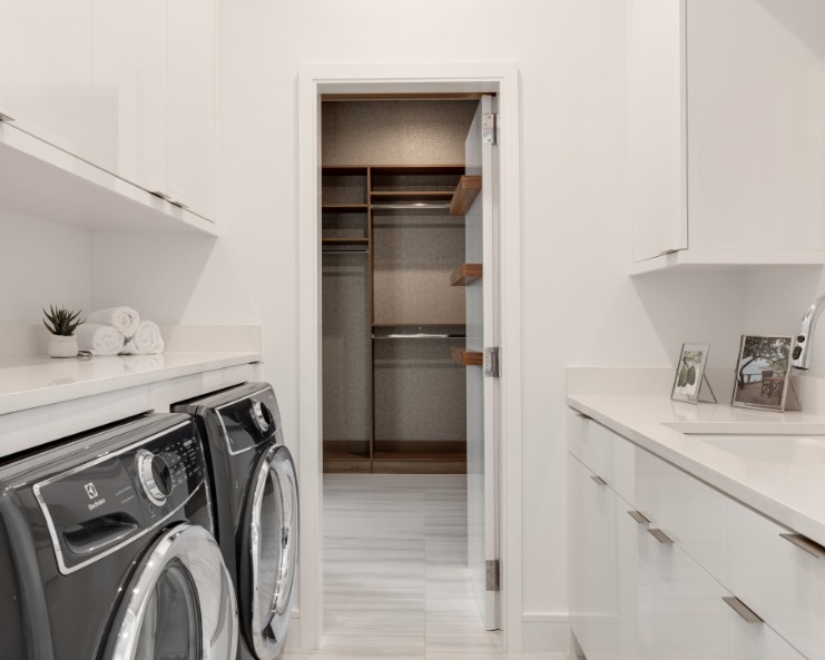 A home's laundry room features white walls, a sink, and a washer and dryer that sit side by side under a counter.