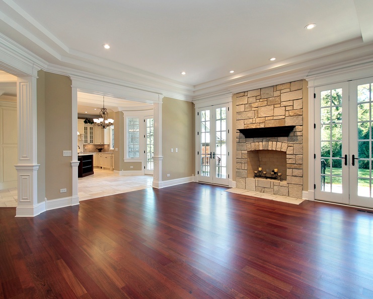 Spacious living room with dark hardwood floors, a stone fireplace, white French doors, and decorative columns.